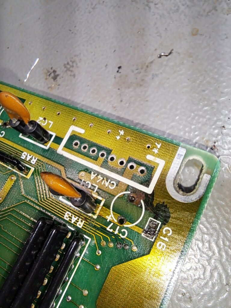 Onderzijde van een synthesizer-printplaat met bruine corrosieschade op het laminaat rondom componentposities — aangetast door uitgelopen condensator-elektrolyt