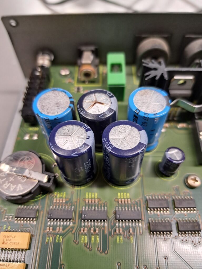 Elektrolytische condensatoren op een synthesizer-voedingsbord — de middelste condensator toont een opgeblazen bovenkant door inwendige drukopbouw