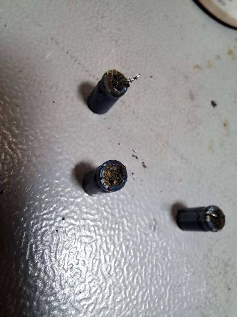 Drie verwijderde elektrolytische condensatoren met opengebarsten bovenkanten en drooggevallen elektrolyt — volledig defect