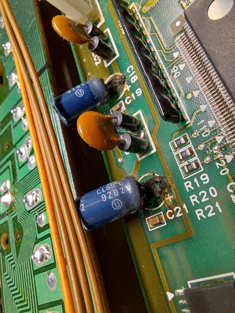 Ernstige elektrolyt-lekkage rondom de voet van een elektrolytische condensator uit 1992 op een synthesizer-printplaat — gedroogd elektrolyt en corrosie op het printmateriaal