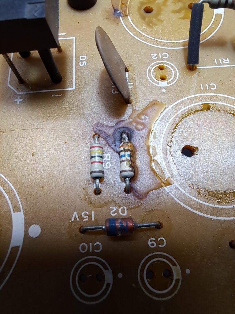Papier-fenolische synthesizer-printplaat met uitgebreide vloeistofschade door condensator-lekkage — het printmateriaal zelf is aangetast, weerstanden R9 en omgeving liggen in de beschadigde zone
