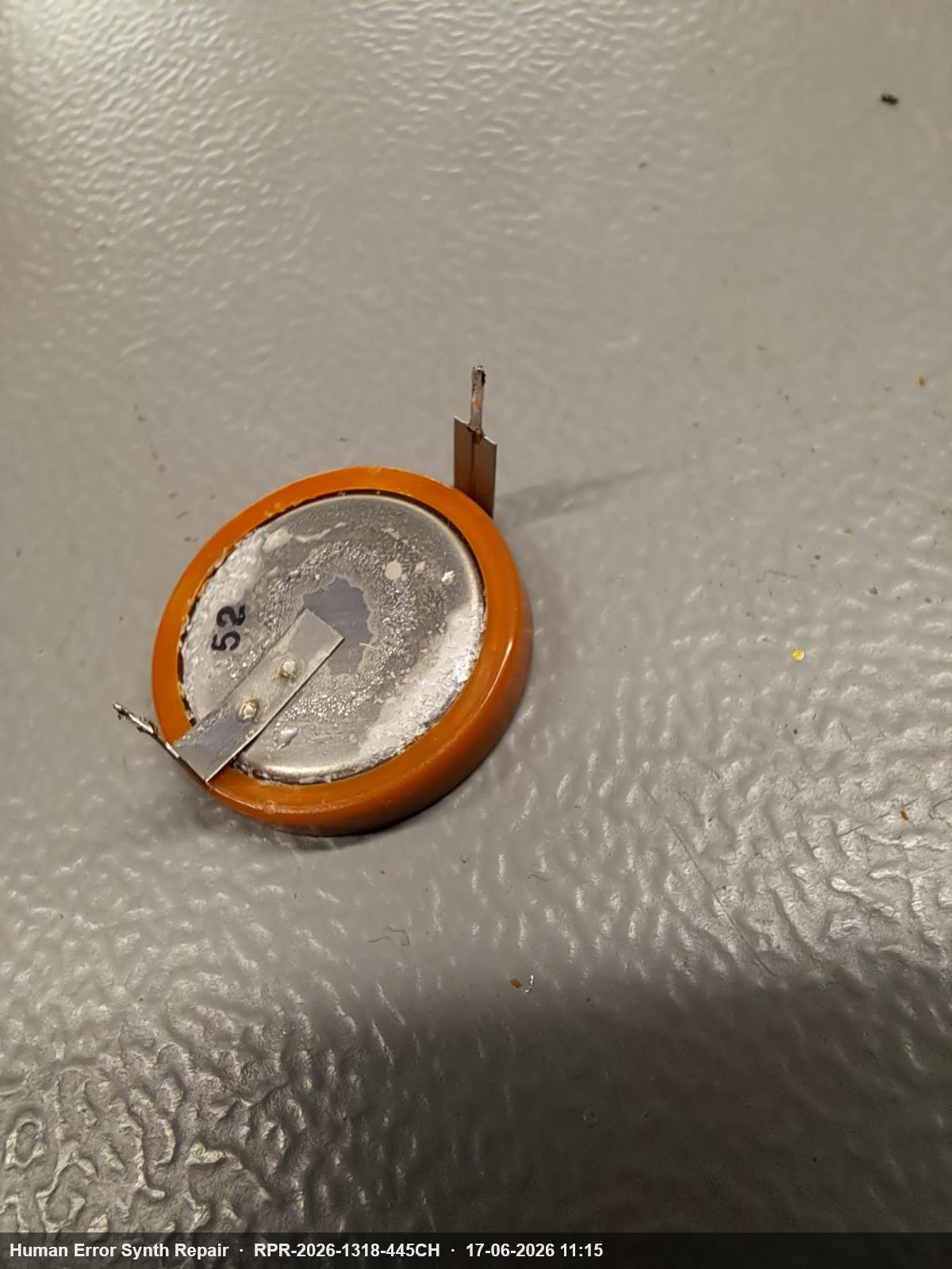 Verwijderde celknoop-backup-batterij met witte corrosieve aanslag over het gehele oppervlak en op de soldeerpennen.