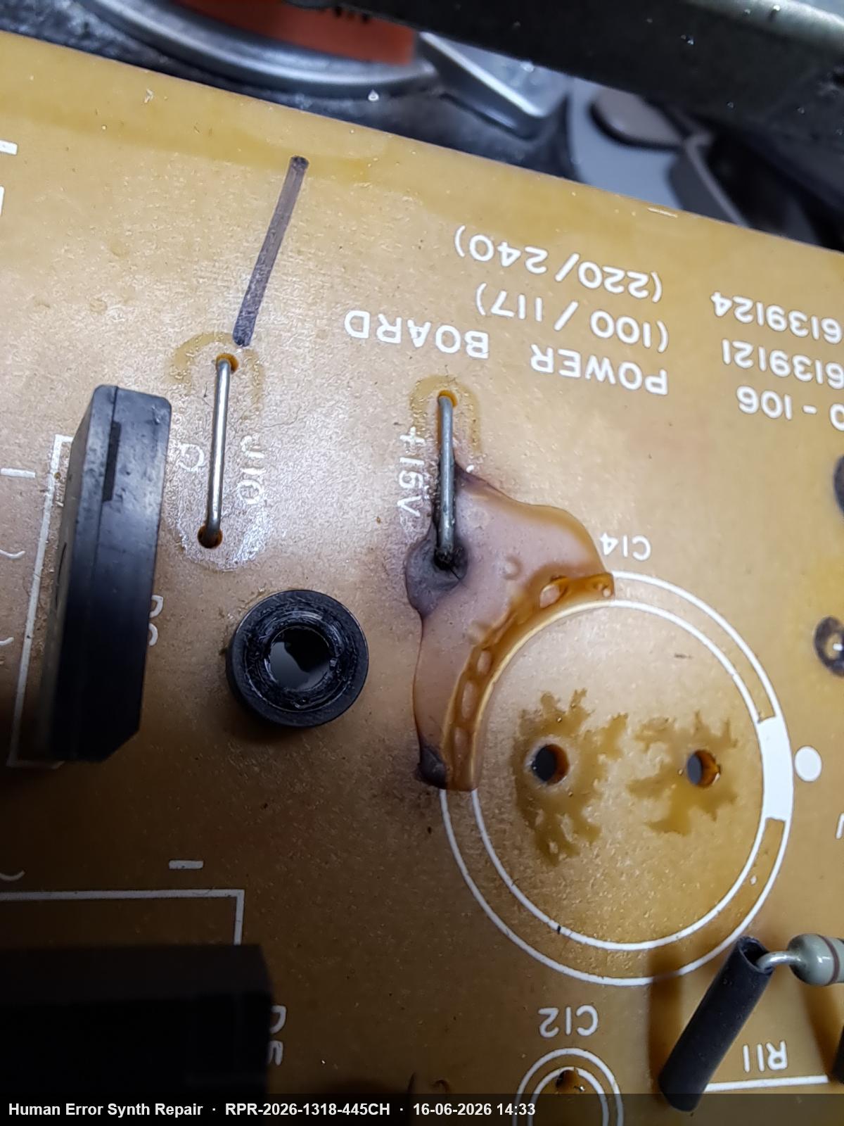 Detail van voedingsplaat bij C14-footprint met ingedroogde bruine vloeistof rondom de condensatorpootjes en de +15V-aansluiting.