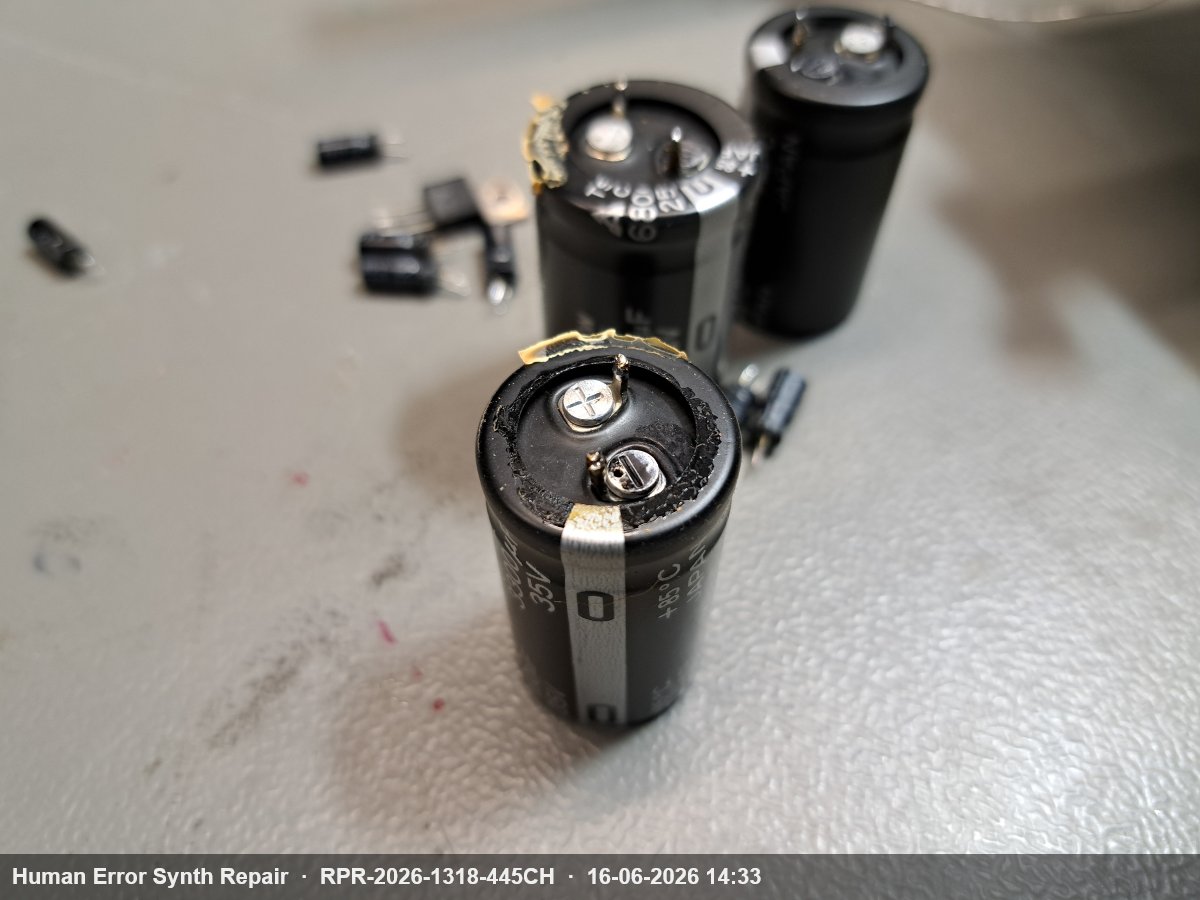 Drie grote elektrolytische condensatoren losliggend op de werktafel, de voorste toont zichtbare ontgassing aan de bovenkant.
