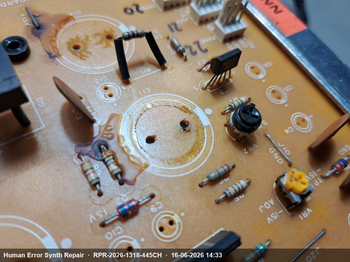 Detail van de voedingsplaat met bruine corrosieve vloeistofsporen rondom de voeten van weerstanden R9 en R8 bij de 15V-lijn.