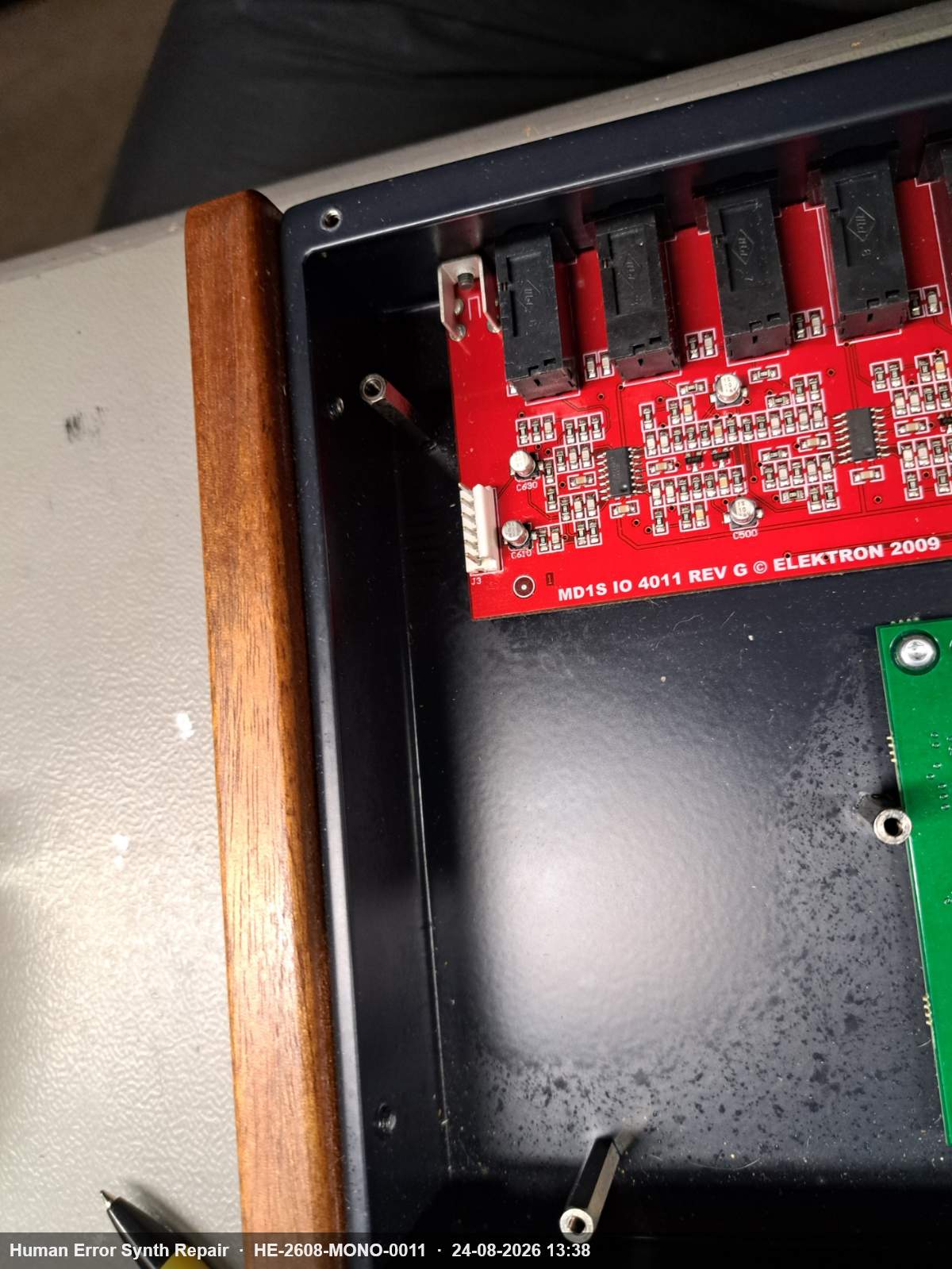 Rode MD1S IO 4011 REV G printplaat in de geopende Monomachine-behuizing met houten zijpaneel zichtbaar.
